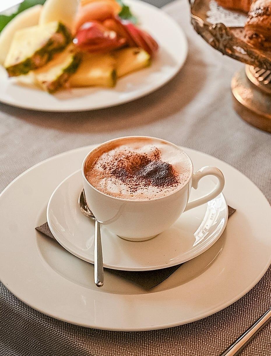 Cappuccino con cacao, frutta fresca e cornetti sull’alzata dorata