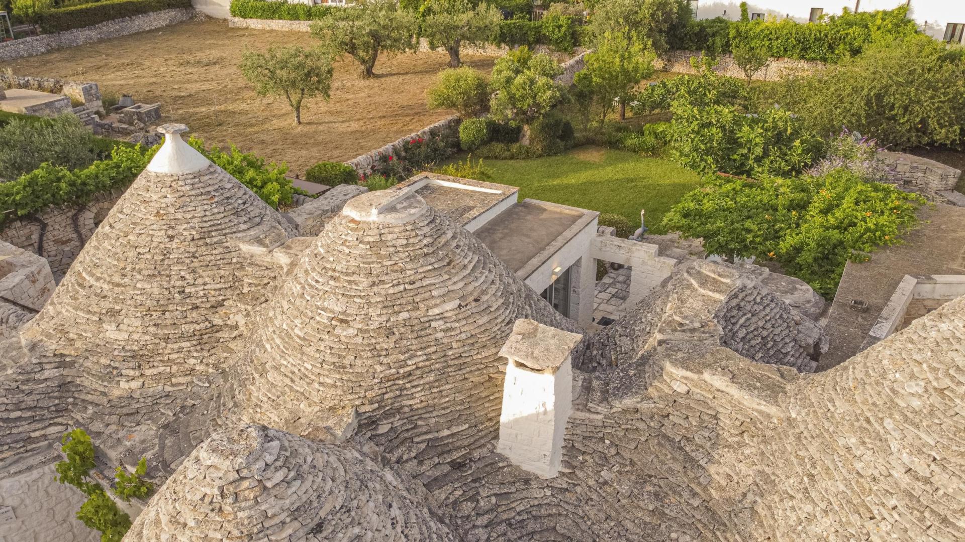 Vista aerea di trulli tradizionali con giardino verde circostante.