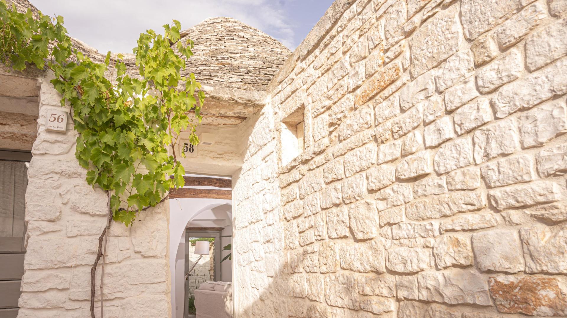 Stone trullo with conical roof and climbing plant, doors numbered 56 and 58.