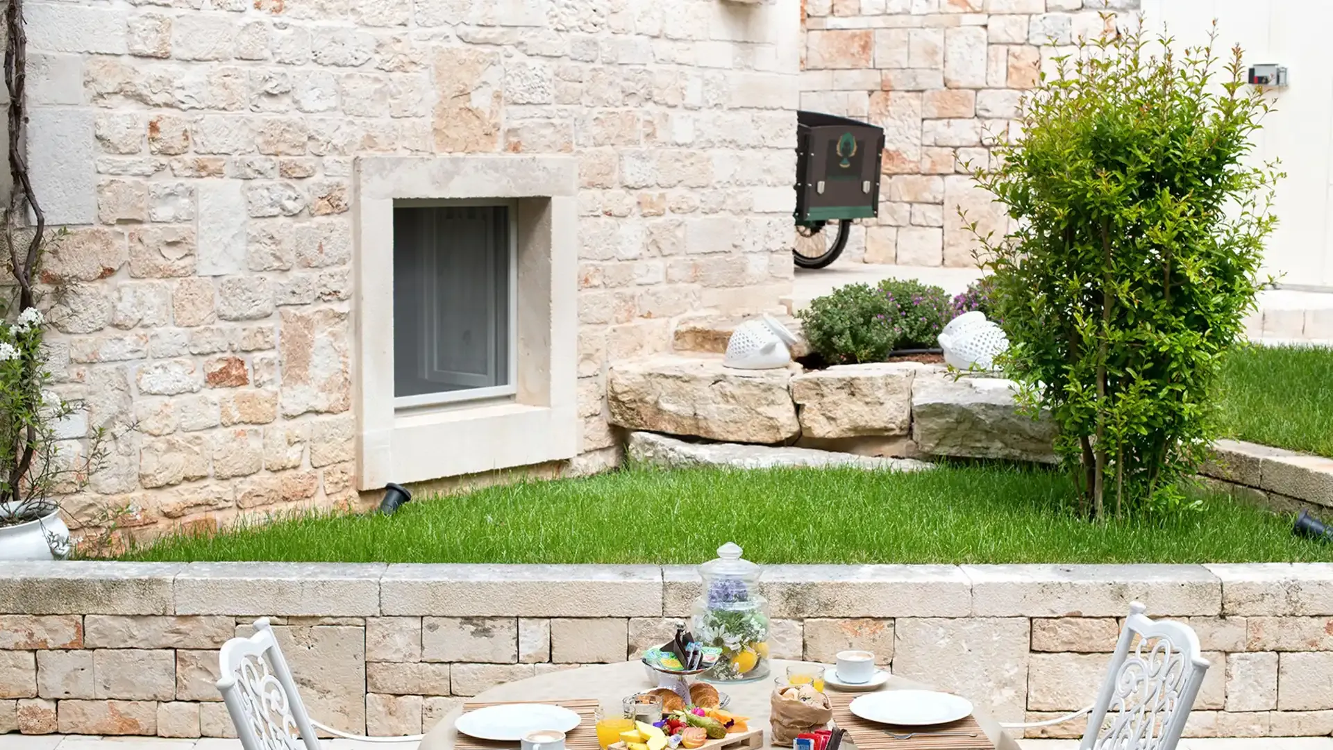 Petit-déjeuner en plein air avec table dressée dans un jardin en pierre.