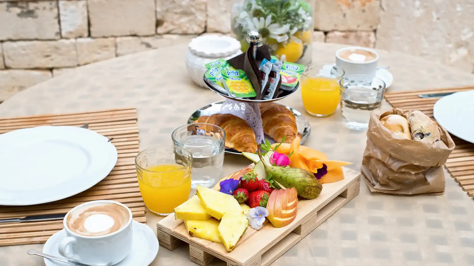 Petit-déjeuner avec fruits frais, croissants, jus d'orange et cappuccino.