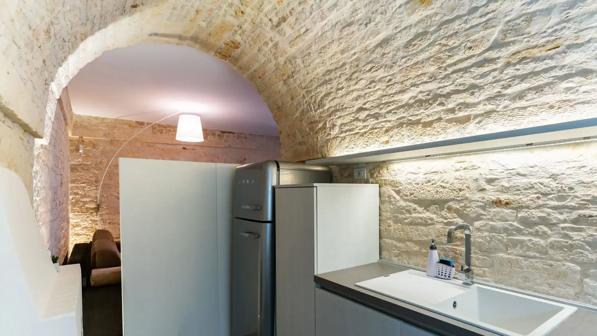 Modern kitchen with stone walls and arched ceiling.