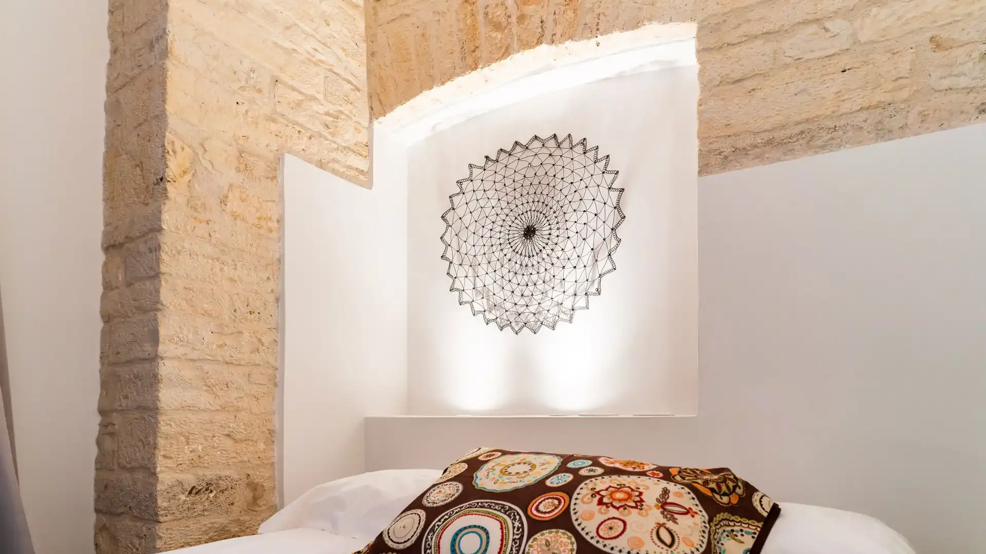 Chambre confortable avec coussin décoré et murs en pierre.