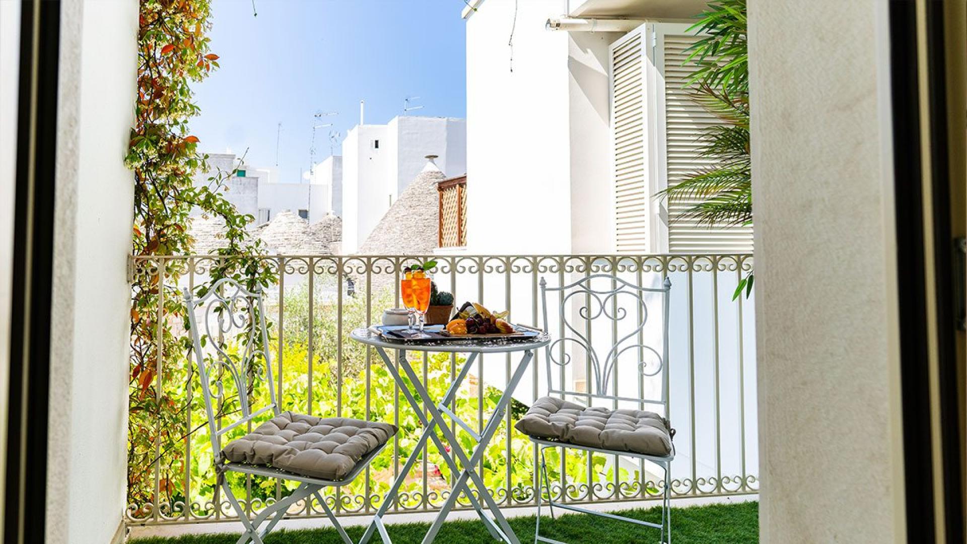 Small balcony with table, chairs, and drinks, overlooking white buildings.