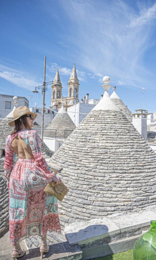 Woman with hat admires the trulli and the blue sky.