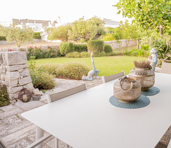 Table de jardin avec décorations, vue sur jardin vert et statues.