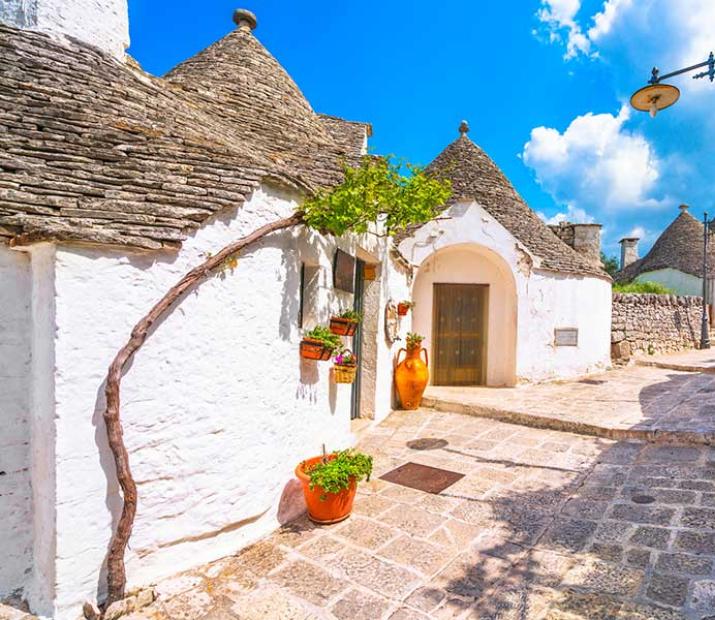 Rue pittoresque avec maisons blanches et toits coniques, typiques des Pouilles.