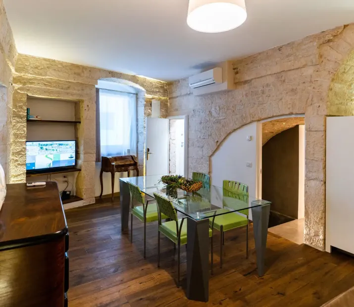 Living room with stone walls, glass table, and green chairs.