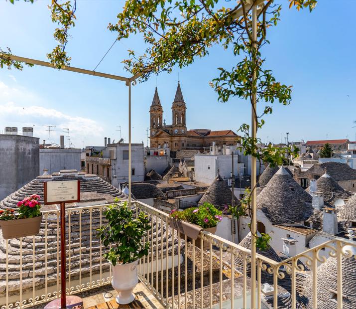 Vue des trulli et de l'église d'Alberobello depuis un balcon fleuri.