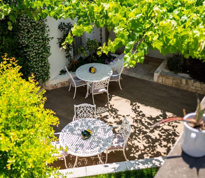 Jardin avec tables et chaises blanches sous une pergola verte.