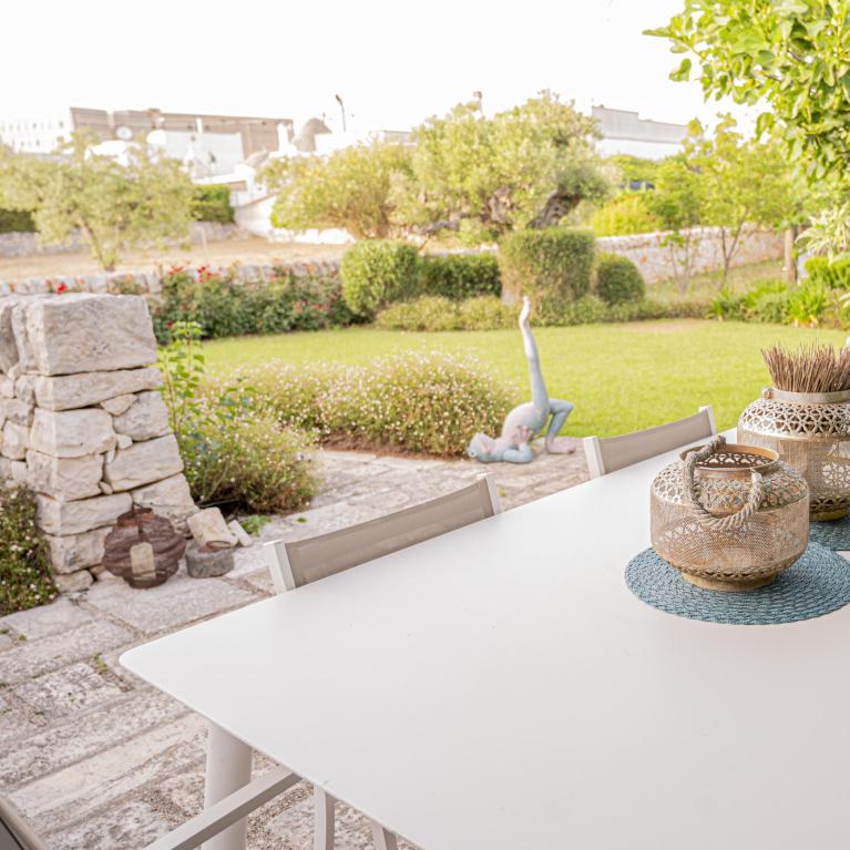 Table de jardin avec décorations, vue sur jardin vert et statues.