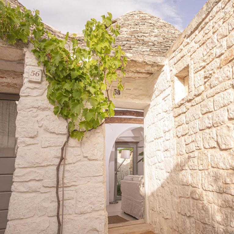 Stone trullo with conical roof and climbing plant, doors numbered 56 and 58.