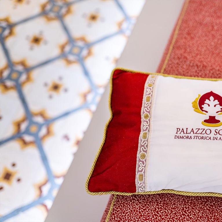 Red decorative pillow with Palazzo Scotto logo, historic residence in Alberobello.