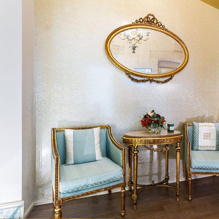 Elegant corner with antique chairs, golden table, and oval mirror.