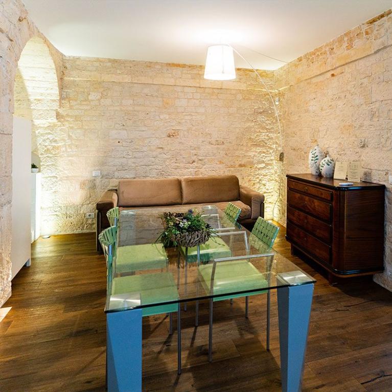 Salon confortable avec murs en pierre, canapé, table en verre et chambre.