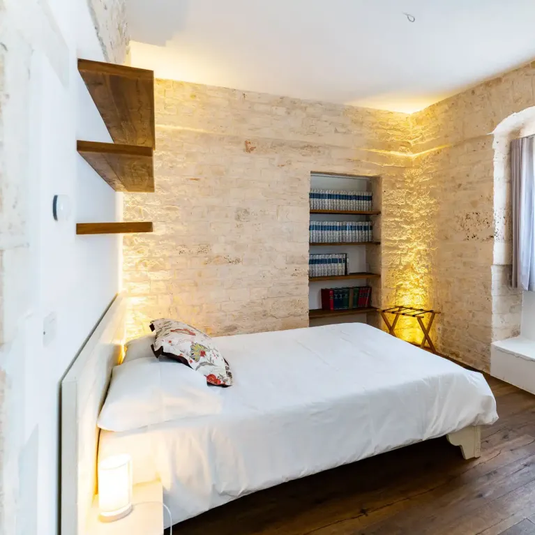 Chambre avec murs en pierre, étagère et fenêtre lumineuse.
