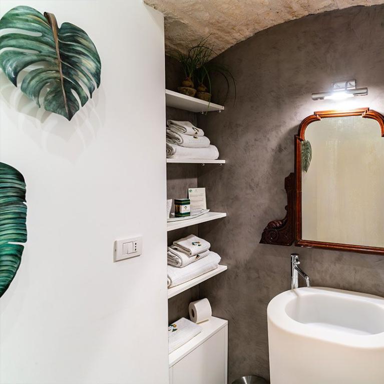Salle de bain moderne avec miroir ancien, lavabo blanc et étagères avec serviettes.