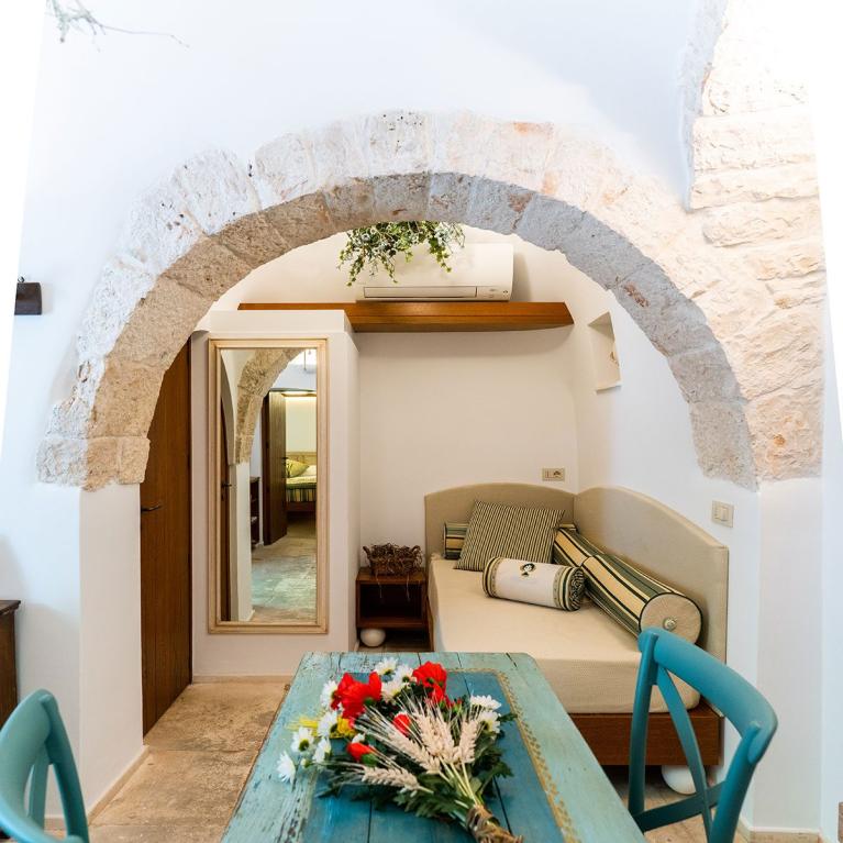 Salon confortable avec table rustique et fleurs, sous une arche en pierre.