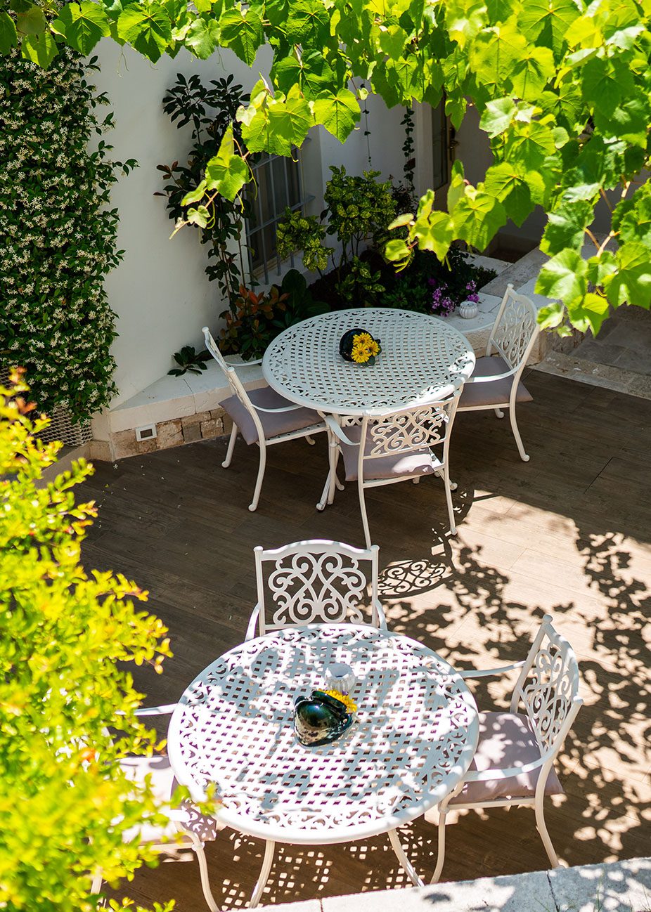 Giardino con tavoli bianchi e sedie circondati da piante verdi.